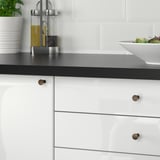 Small, round, bronze NYDALA knobs on sleek white kitchen drawers, enhancing cabinet style, contrasting minimalist design.