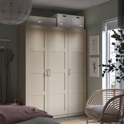 Modern bedroom with beige PAX wardrobe, double doors, built-in lights, hanging rack, dark green walls, chair, art prints.