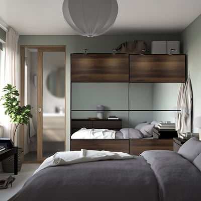 Bedroom with large PAX wardrobe, sliding glass doors, neatly arranged clothes, comfortable bed, side table with plant and basket.