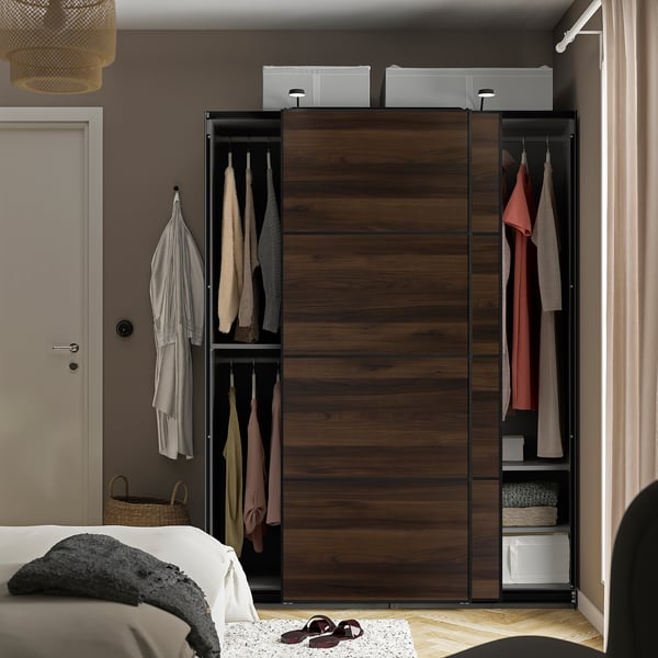 Modern bedroom with a PAX wardrobe featuring sliding doors, hanging clothes, and adjustable feet for floor levelling.