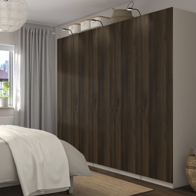 Bedroom with dark wooden PAX wardrobes, mesh baskets, soft-close hinges, and decorative lights. Bed partially visible.
