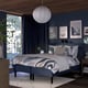 Grey RÅHOLMAR bed with abstract bedding, dark blue walls, large windows, wooden nightstands, white pendant lamp.