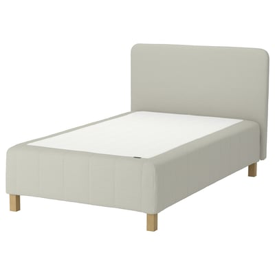 Depicts a light grey RÅHOLMAR bed with a padded headboard, wooden legs, and a flat surface.