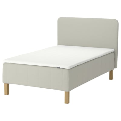 RÅHOLMAR bed in beige fabric with wooden legs, featuring 5 comfort zones and a soft headboard for relaxed reading or tv watching.