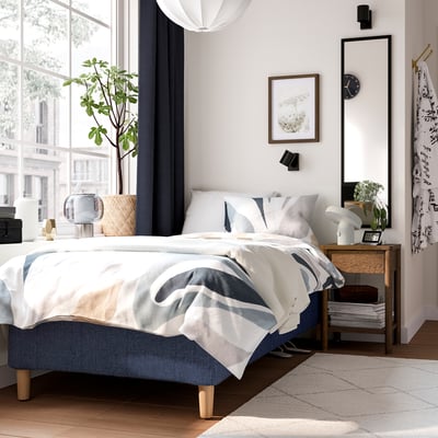 Modern bedroom with RÅHOLMAR bed, blue & wooden, natural light, nightstands with lamps, minimalist decor, plant, airy.