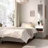 Minimalist bedroom with white bed, large window, mirror, wooden bedside table, plants, and chandelier.