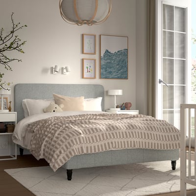 Grey upholstered bed with striped bedding, art, and chandelier; larger than crib.