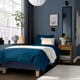 Modern bedroom with teal bed, dark blue wall, wooden bedside table, large window, mirror, and hanging light.