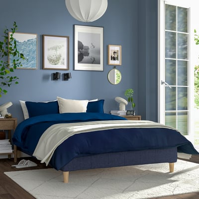 Blue bedroom with RENFJÄLLET bed, featuring wooden headboard, blue bedding, wall art, and a white rug. A window lets in natural light.