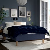 Modern blue bedroom with RISHÖJDEN bed, dark blue chequered bedding, art, light wood legs.