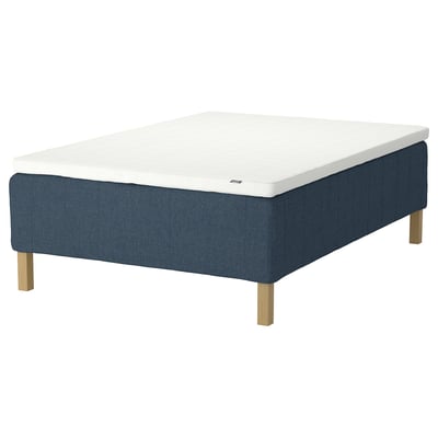 The rishojden bed base is blue, rectangular, upholstered with fabric, has wooden legs, and a white mattress pad on top.