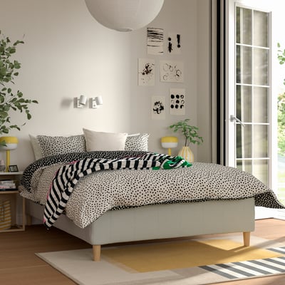 Bedroom with RISHÖJDEN bed, black/white bedding, yellow lamp, rug, art on white walls.