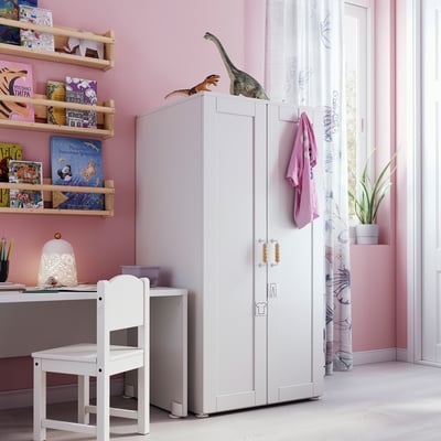 Kids room with pink walls, white furniture, dinosaur toys, books, and desk.