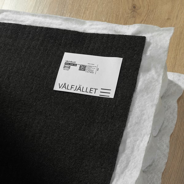Black IKEA mattress roll with white tag reading VÅLFJÄLLET on wooden floor.
