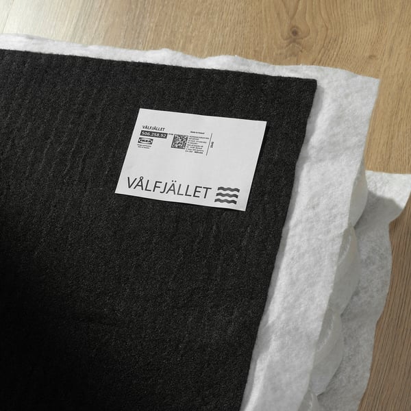 Black IKEA mattress rolled up on a wooden surface with a white label reading VÅLFJÄLLET and a qr code.
