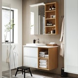Modern white bathroom with ÄNGSJÖN vanity, open shelf, large mirror, black stool, glass shower door.
