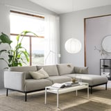 Modern living room with light grey ÄPPLARYD sofa, white coffee table, large plant, and hanging light.