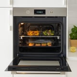 Open stainless steel oven with glass door shows multiple dishes cooking. Digital display, touch control, and convection cooking visible.