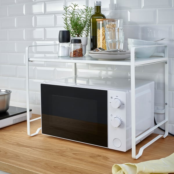 White kitchen organiser rack above microwave, holding cups, bowls, spices, and a plant.