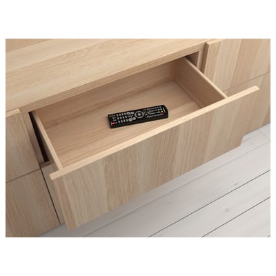 Light wood drawer with black remote control, part of the BESTÅ system.