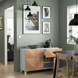 Modern sideboard with shelves & drawers against green wall. White countertop with bowl & coffee accessories. Wooden chairs & hangings.