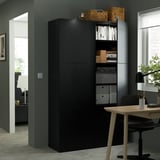 Black storage unit with adjustable shelves, holding books and office supplies, next to a wooden desk in a modern office.