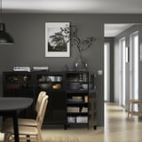 Modern dining room with black BESTÅ sideboard, displaying dishes and decor, beneath framed nature photo.
