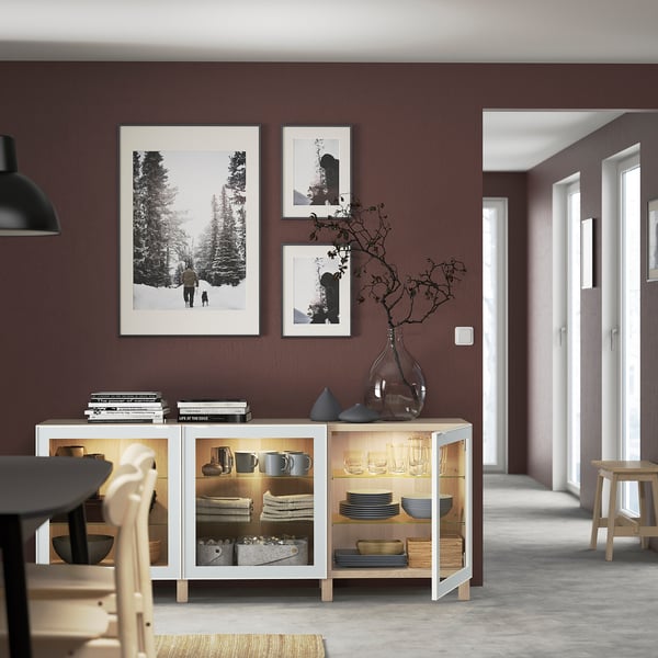 Modern dining room with maroon walls, illuminated sideboard displaying dishes and vases, two wall photos.