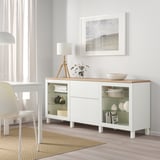 White BESTÅ sideboard with glass doors, lamp, and plant. Modern design.
