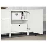 White BESTÅ sideboard with adjustable shelves, drawers, and soft-closing function. One door open, showing storage boxes and books.