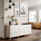 Modern living room with BESTÅ sideboard, wood accents, black pendant lamps, and decor. Sideboard has photos, vase, bowl, inviting seating area.