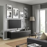 Modern living room with BESTÅ tv bench in black, featuring a flat-screen tv, surrounded by framed photos, a tall lamp, and a glass coffee table.