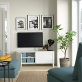 Modern living room with BESTÅ tv bench, cables managed, black tv, photos, green plant, blue chairs.