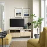 Modern living room with BESTÅ tv bench, tv, mountain photos, yellow sofa, and green plant.