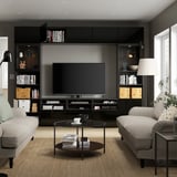 Modern living room with black BESTÅ tv unit, grey sofas, round coffee table, stacks of books, decorative items, and recessed lighting.
