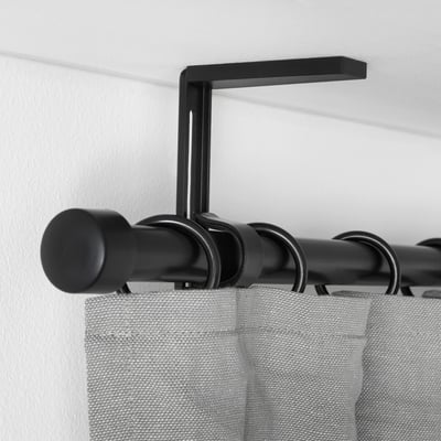Black curtain rod holder mounted on white wall, holding black rod with grey curtains, demonstrating adjustable positioning.