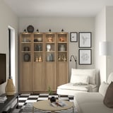 Modern living room with BILLY bookcase, decorative items, white sofa, black lamp, art prints, checkerboard rug, and coffee table.