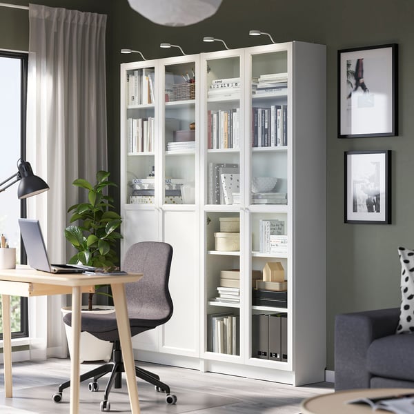 Modern home office with large BILLY white bookcase, grey chair, desk, laptop, and large windows with curtains.