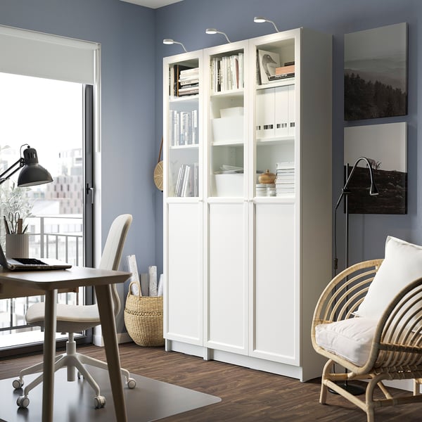 BILLY bookcase with books & decor, beside door & desk, tall, near wicker chair.