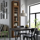 Modern dining area with BILLY bookcase, black table, green chairs, large window, pendant lamp.