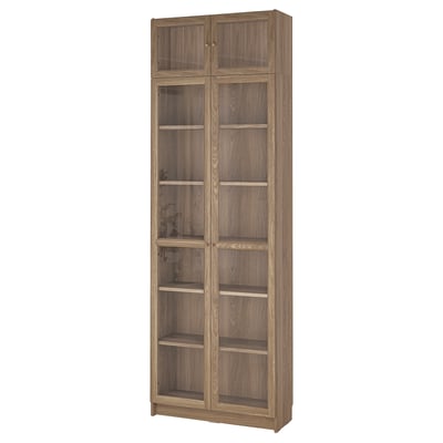 An empty wooden bookcase named BILLY. It multiple shelves with glass doors. The colour is light brown.