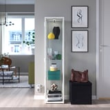 BLÅLIDEN cabinet with books and decor, spotlighted top shelf, green sofa, large windows.