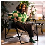 Person sits in BRÄNNBOLL chair, wearing headphones, laughing, with laptop on lap, perfectly blending comfort and style in a cosy, indoor setting.