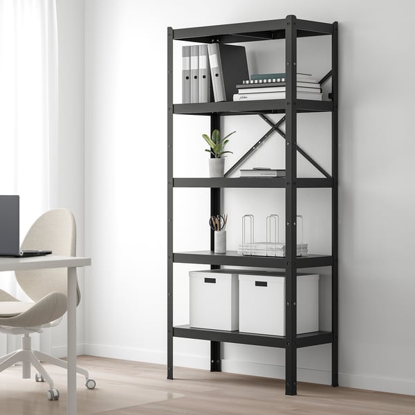 Black BROR shelving unit in minimalist office, holding books, boxes, and a plant.