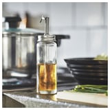 Glass CITRONHAJ oil dispenser with steel spout on counter by stove & cutting board with onions.