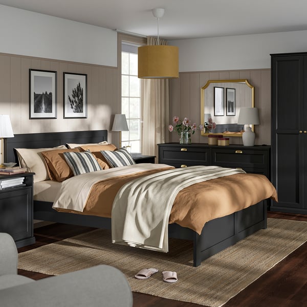 Modern bedroom with black bed, beige bedding, matching furniture, wall art, rug, and pendant light.