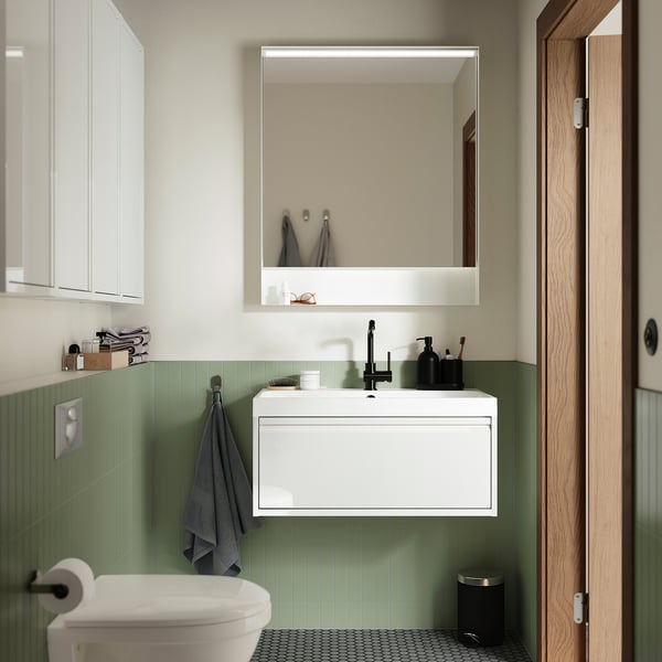 Modern bathroom with FAXÄLVEN mirror, soft light, reflecting toilet & sink, above cabinet.