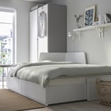 Modern bedroom with FLEKKE sofa-bed, drawers, light grey linens, closet, & wall shelf with decor.