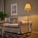 Warm, lit floor lamp next to a grey couch. Tall, cone-shaped shade, versatile design.