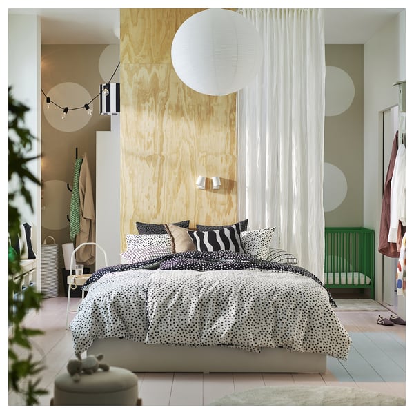 Modern bedroom with wooden accent wall, polka dot bedding, white curtains, hanging lights, and green crib.